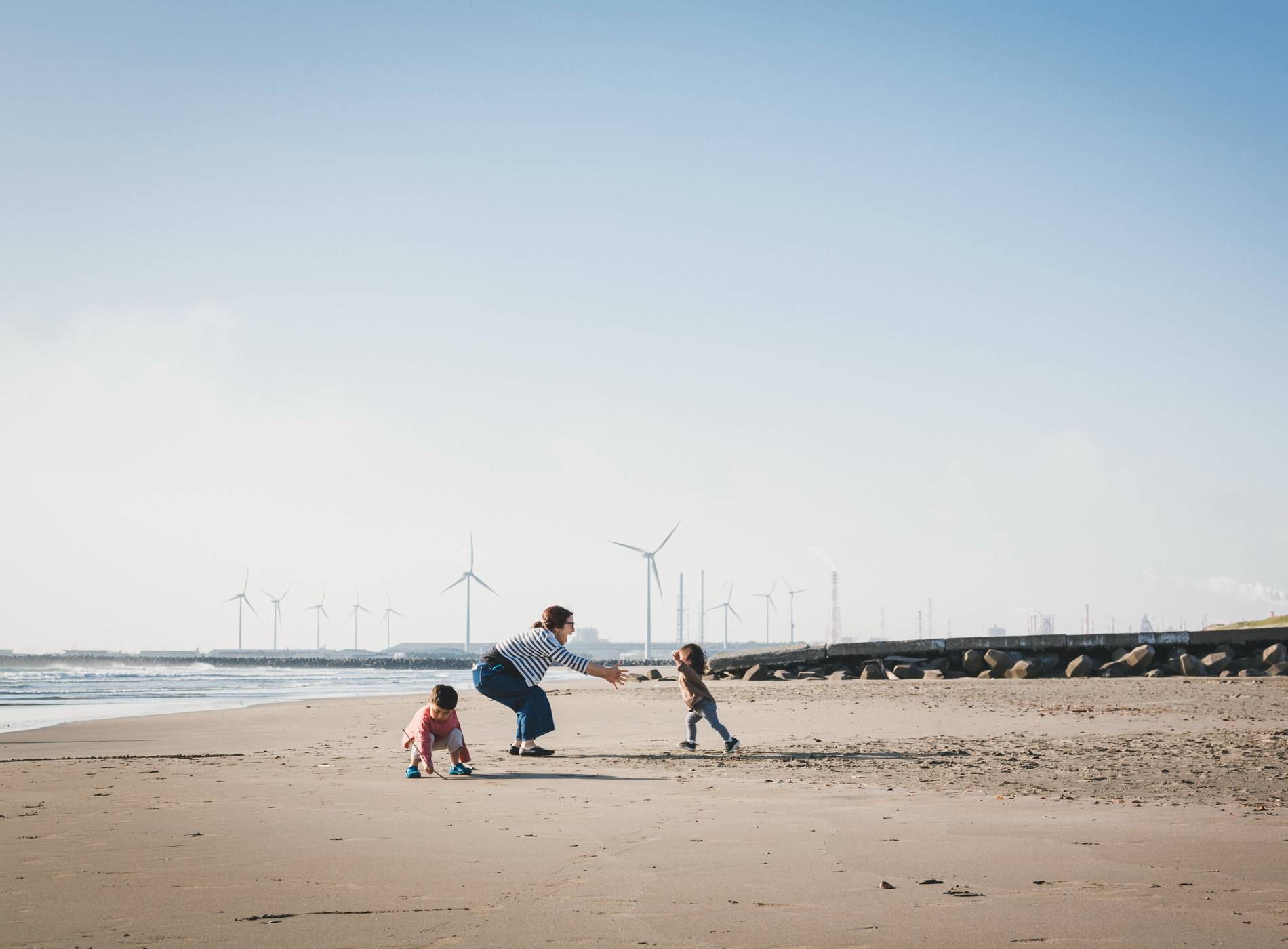 Asian family playing in the beach where there is wind power station in the background.