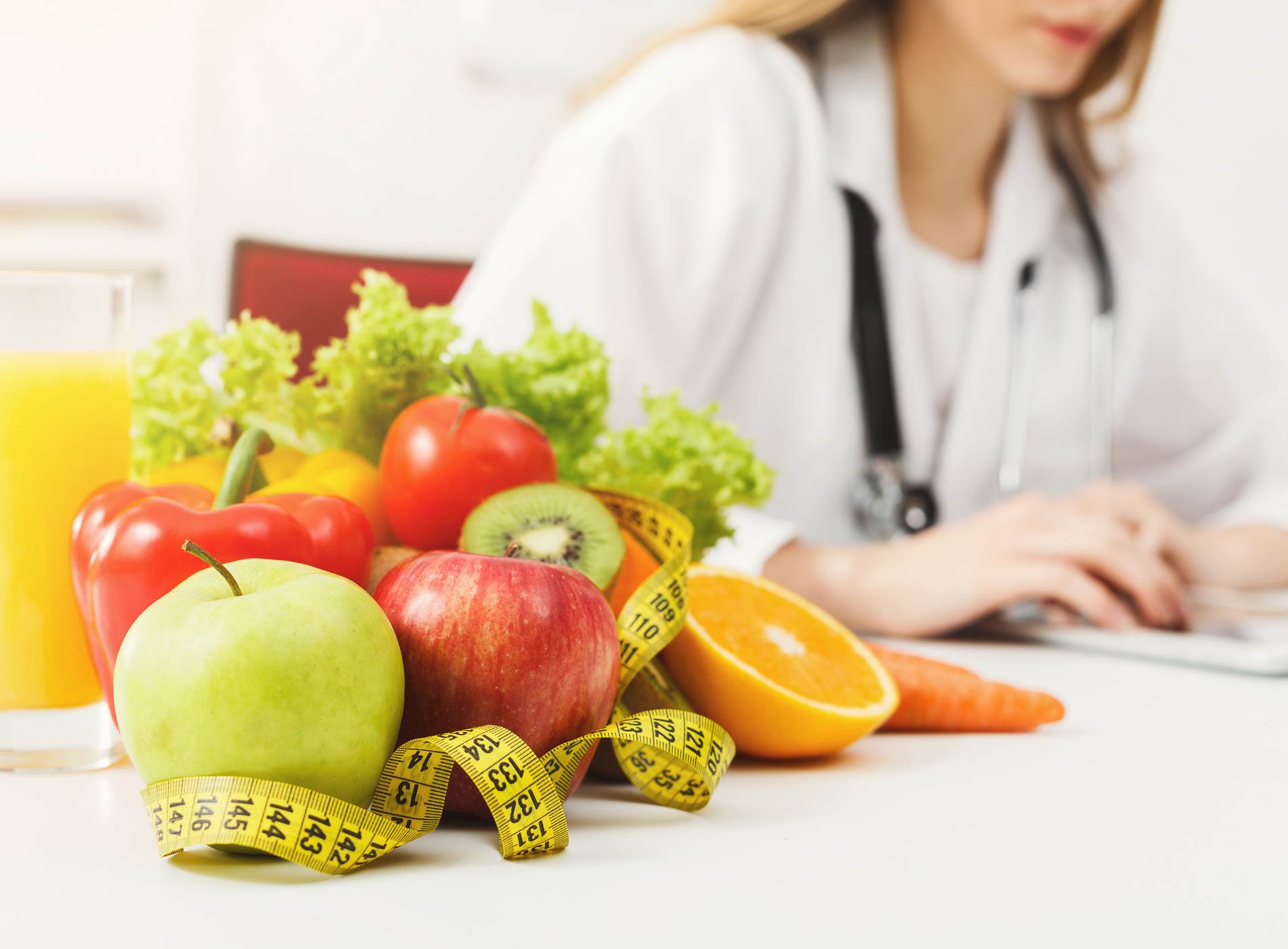 Nutritionist desk with healthy fruit, juice and measuring tape. Dietitian working on diet plan. Weight loss and right nutrition concept