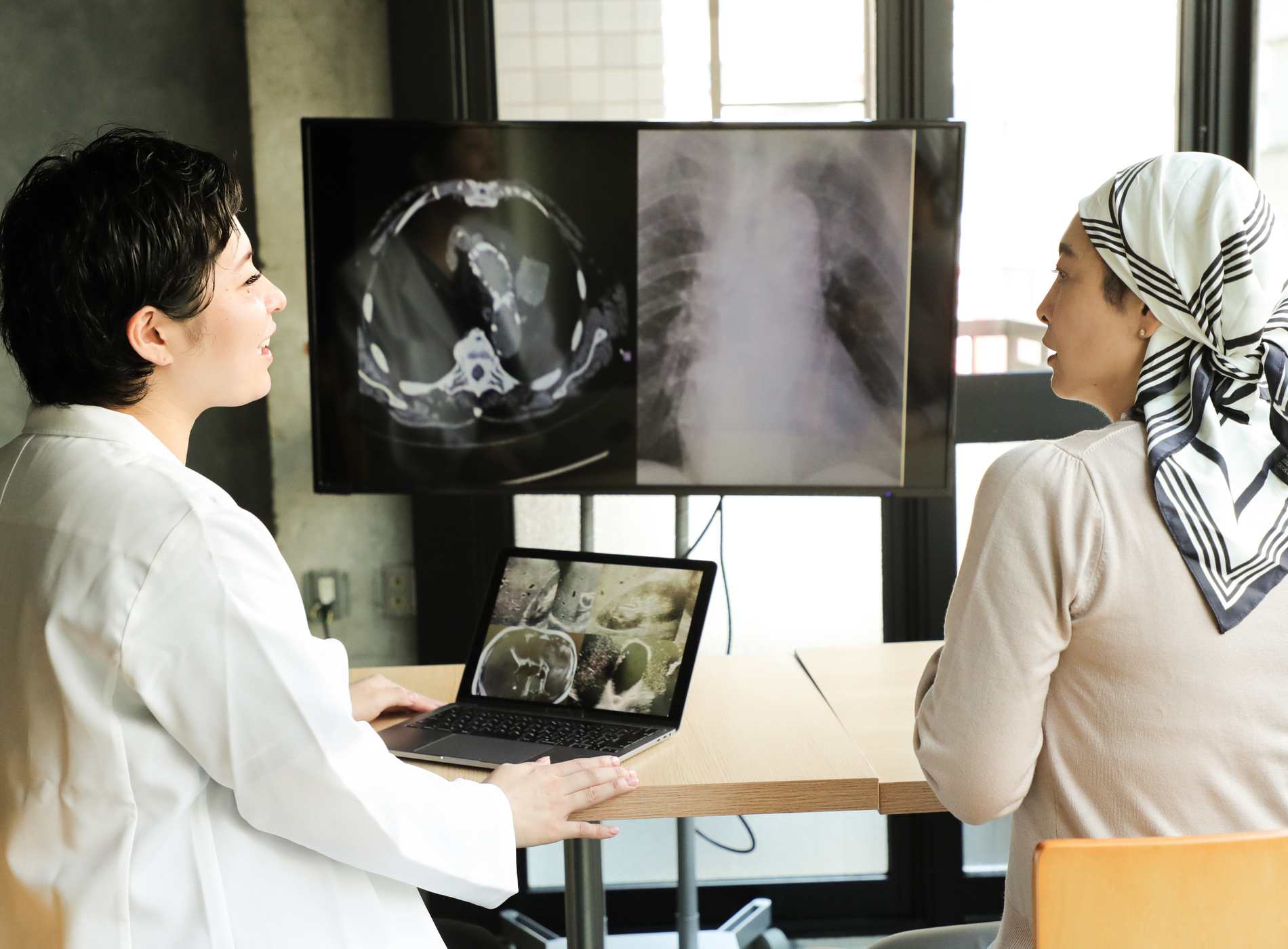 Doctors talk to cancer patient in a hospital counseling room about the progression of her disease. They look CT scans, echoes and MRI images. They talk in depth about the treatment plan and the future.