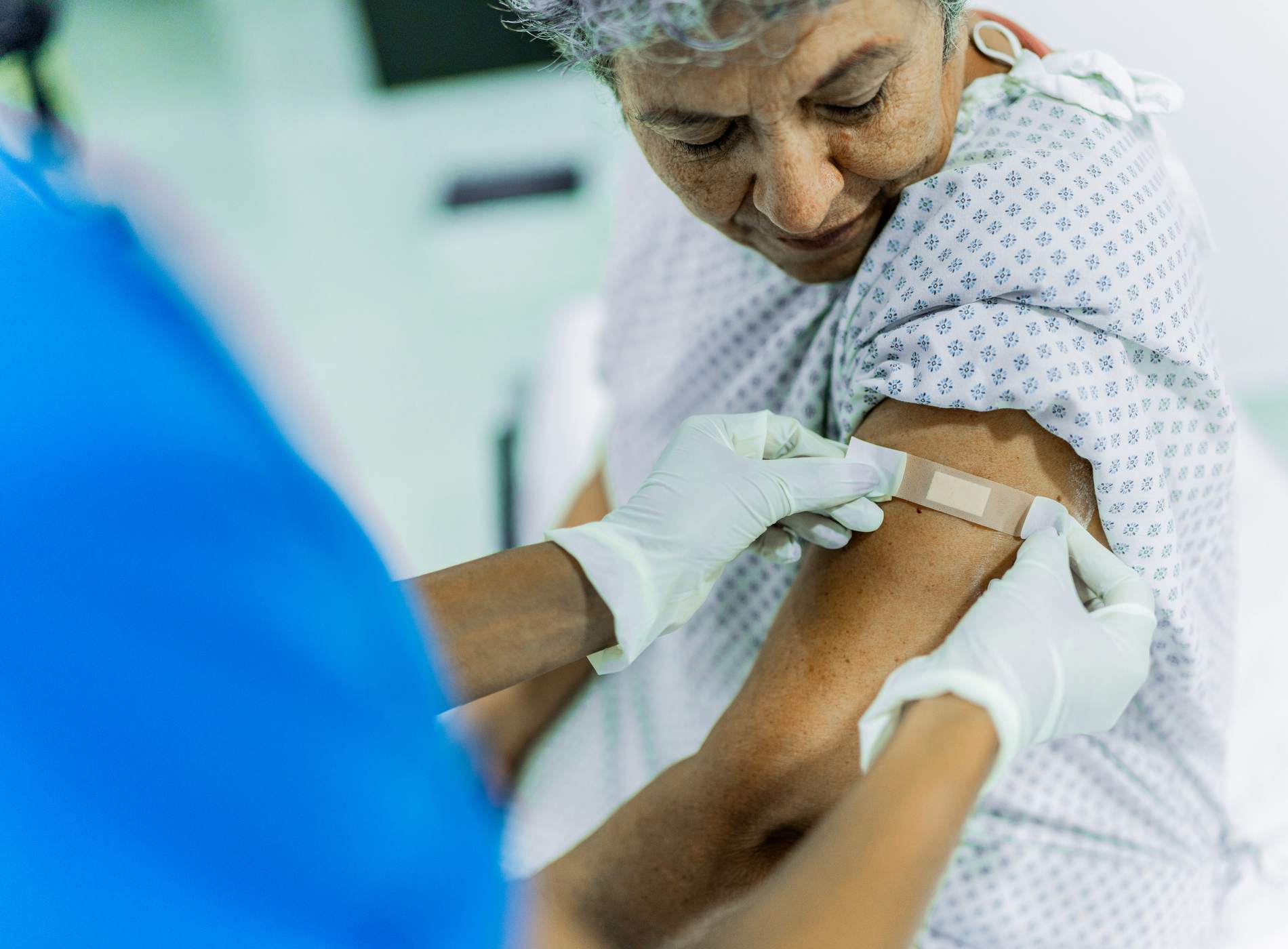 Female nurse putting adhesive bandage on senior woman pacient's arm after vaccination at the hospital