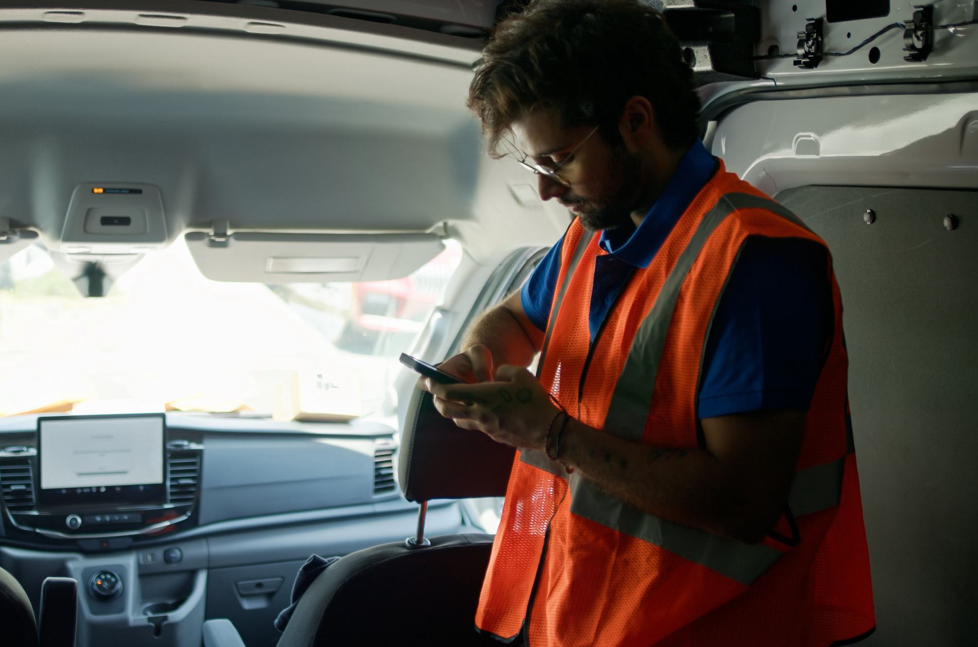 A young, Indian delivery person using his phone inside his delivery van during a shift on a sunny day in Los Angeles, California.