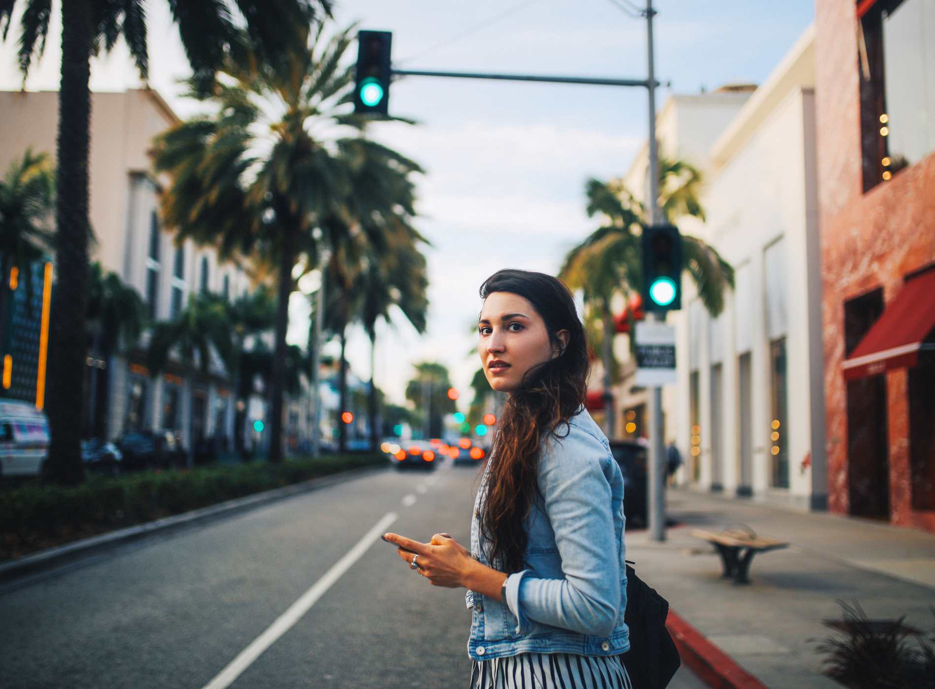 Young woman walking the streets of Los Angeles - West Hollywood - Beverly Hills area, texting on her smartphone, checking messages or trying to catch a ride share transportation.